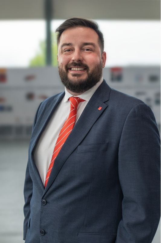 Smiling man with short dark brown hair and short beard with blue suit